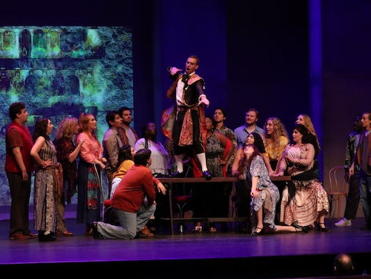 Group of people on stage with one person elevated.