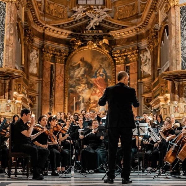 The back of a man conducting an orchestra in a church.