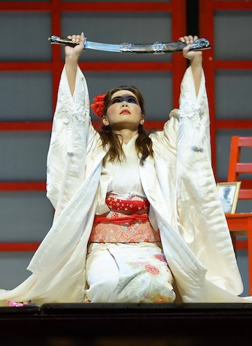 Woman on her knees in a kimono with a sword held high over her head.