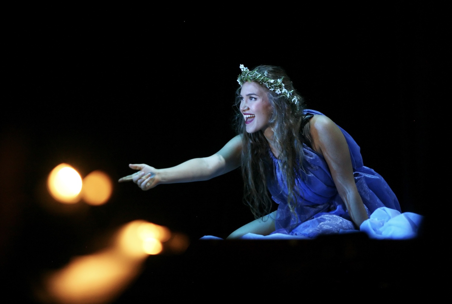 Woman with a crown of leaves smiling on her knees, reaching towards orbs of light