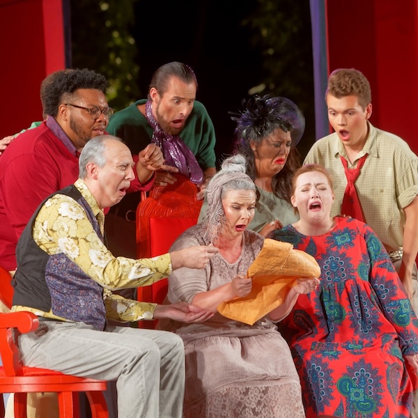 Woman in the center holding a parchment surrounded by a group of shocked people.